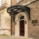 Semi‑circular outdoor glass awning with ornate wrought iron scrollwork.