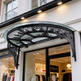 Semi‑circular outdoor glass awning with ornate wrought iron scrollwork.