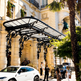 Curved rectangular glass canopy with ornate wrought iron scrollwork and dual lanterns.