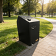 Black trash bin on a sidewalk in a park