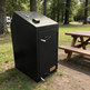 Black smoker grill on a grassy area with picnic table and trees in the background