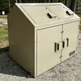 Beige metal storage cabinet with two doors on a gravel surface with trees in the background
