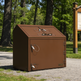 Brown metal trash bin in a park setting with trees and a sign in the background