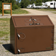 Brown metal cabinet with multiple outlets on a gravel surface, with RVs in the background.