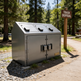 Metal trash disposal unit in a forested area with a 'Trash Disposal' sign.