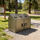 Metal trash bin in a park setting with trees and picnic tables in the background
