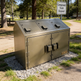 Metal trash disposal unit in a campground with a 'Campground Trash Disposal' sign in the background.