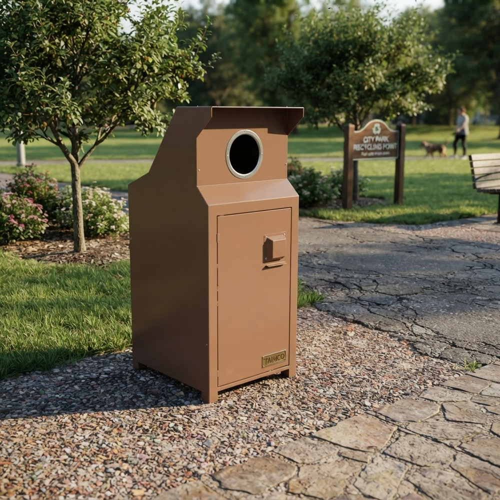 A brown metal trash can with a circular opening on top, set on a stone path in a park with trees and grass in the background.