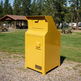 A bright yellow TAIMCO outdoor storage cabinet with a top mail slot and front door handle, photographed on a gravel path at a grassy campsite with trees and picnic areas in the background.