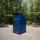 A blue metal trash compactor or dumpster container with a small 'TANCO' brand plate, situated on a gravel path in a wooded outdoor setting.