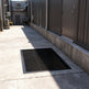 Black steel round‑bar window well grate installed over a gravel‑filled basement window well with a concrete border.