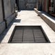 Black steel round‑bar window well grate installed over a gravel‑filled basement window well with a concrete border.