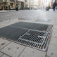 Metal manhole cover on a city sidewalk with pedestrians in the background