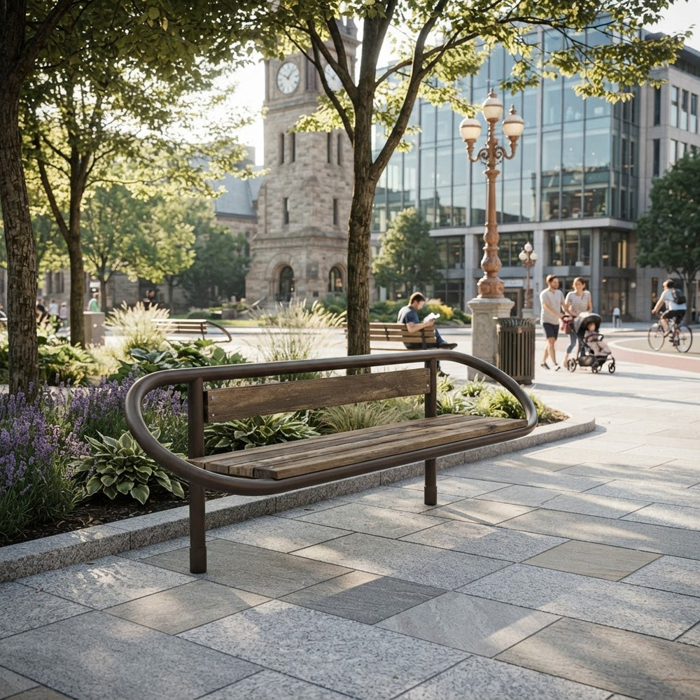 A modern wooden park bench with a curved metal frame sits on a paved plaza in a sunny urban park. Trees, landscaped beds, a clock tower building, and pedestrians are visible in the background.
