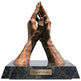 Bronze sculpture of praying hands on a marble base with 'Unity in Devotion' plaque.