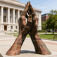 Bronze sculpture of interlocked hands in front of a classical building
Bronze statue of clasped hands with detailed veins and natural form